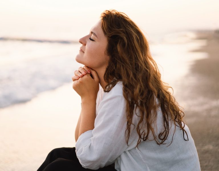 girl with eyes closed and hands under her chin sitting peacefully by the beach